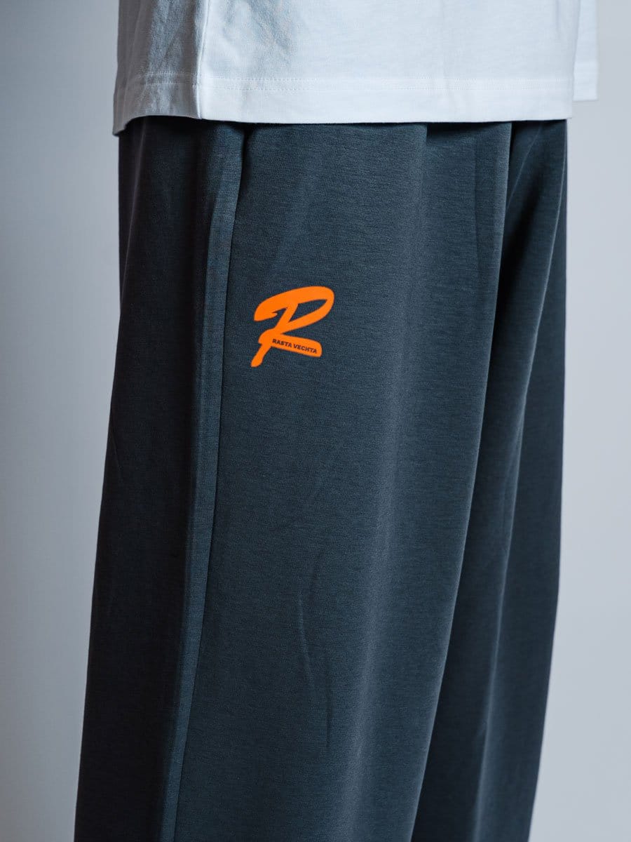 Dunkle Sports- oder Jogginghose mit orangefarbenem Logo auf der linken Seite, aus weichem Material, getragen von einer Person.