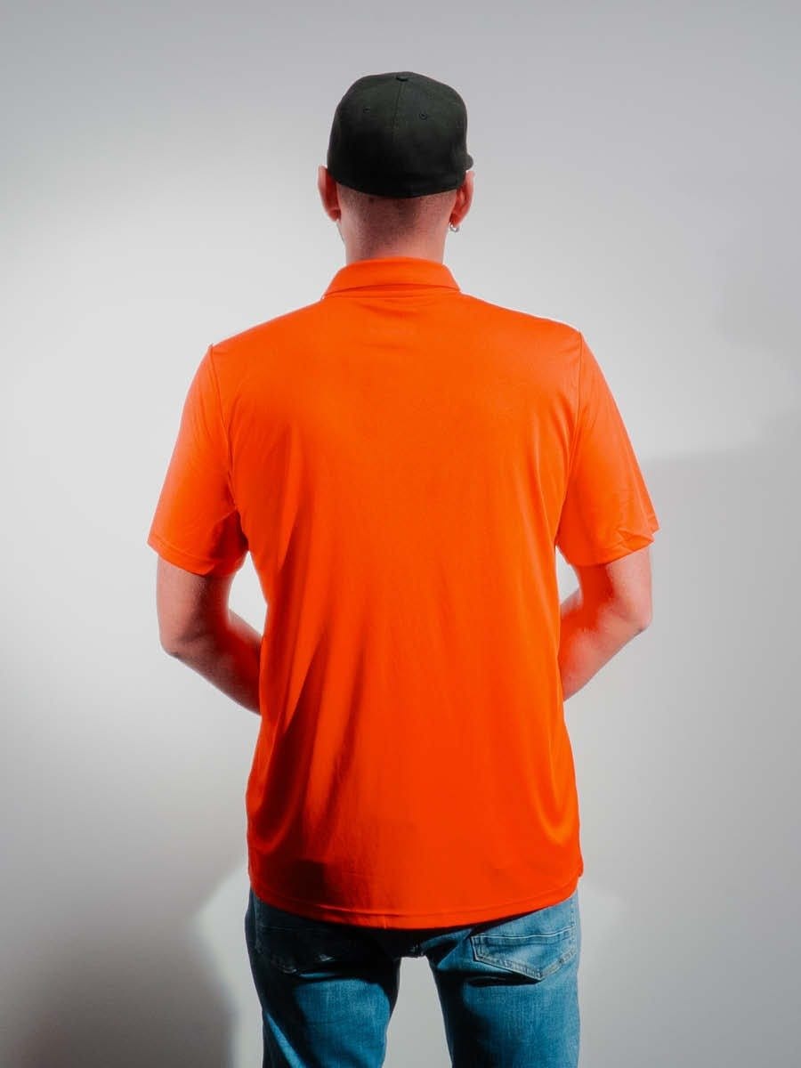 Mann trägt orange T-Shirt, schwarze Mütze, blaue Jeans, steht vor neutralem grauem Hintergrund, Rückenansicht.