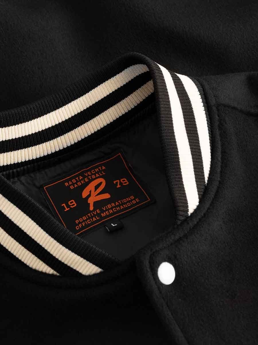 Nahaufnahme eines schwarzen Varsity-Jackenkragens mit weiß-schwarzem Streifenmuster und einem Etikett mit roten und schwarzen Schriftzügen.
