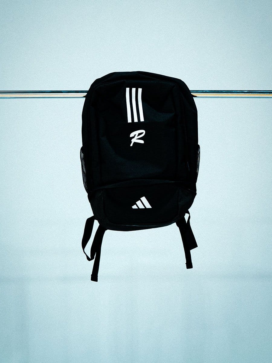 Schwarzer Rucksack mit weißen Markenlogos, hängt an einer horizontalen Stange vor hellem Hintergrund.