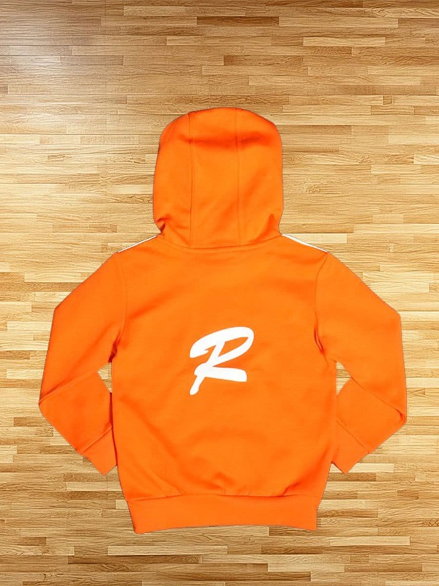 Orangene Kapuzenjacke mit weißem Logo auf dem Rücken, liegt flach auf einem Holzboden.