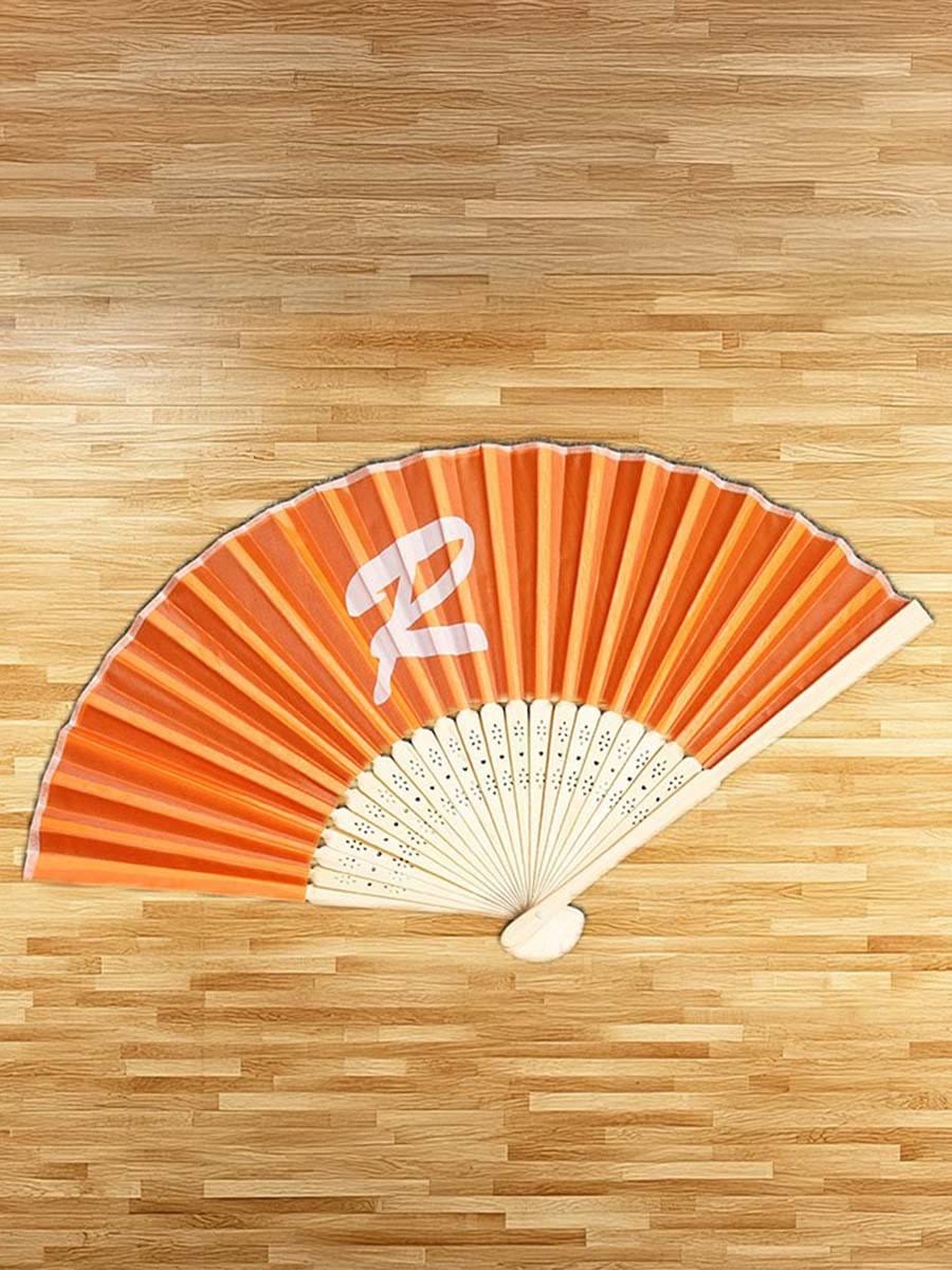 Fächer mit orange-weißer Gestaltung, liegend auf einem Holztisch, mit der Zahl 2 in weiß auf orange.