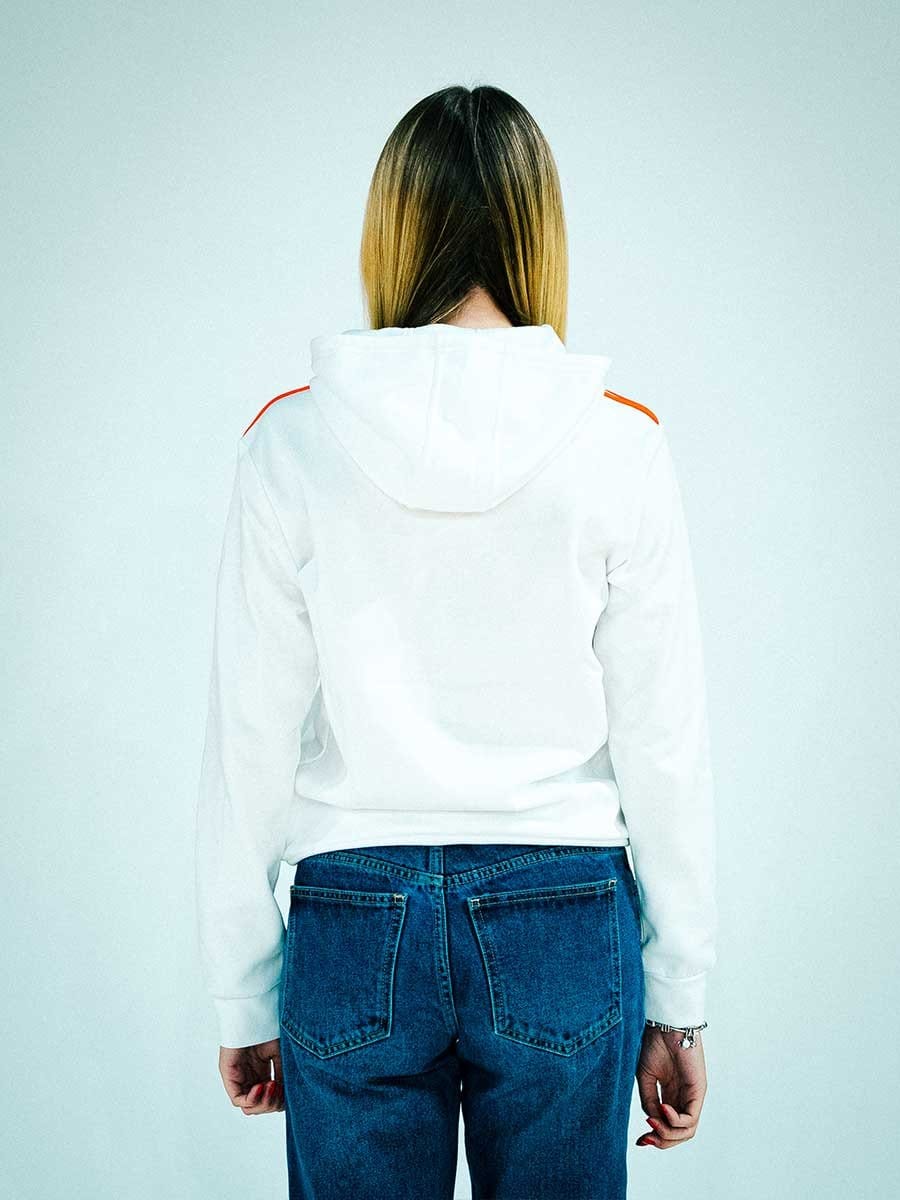 Rückansicht einer Person mit braun-blondem Haar, die eine weiße Kapuzenjacke trägt und ihre Hände seitlich hängen, vor hellem Hintergrund.