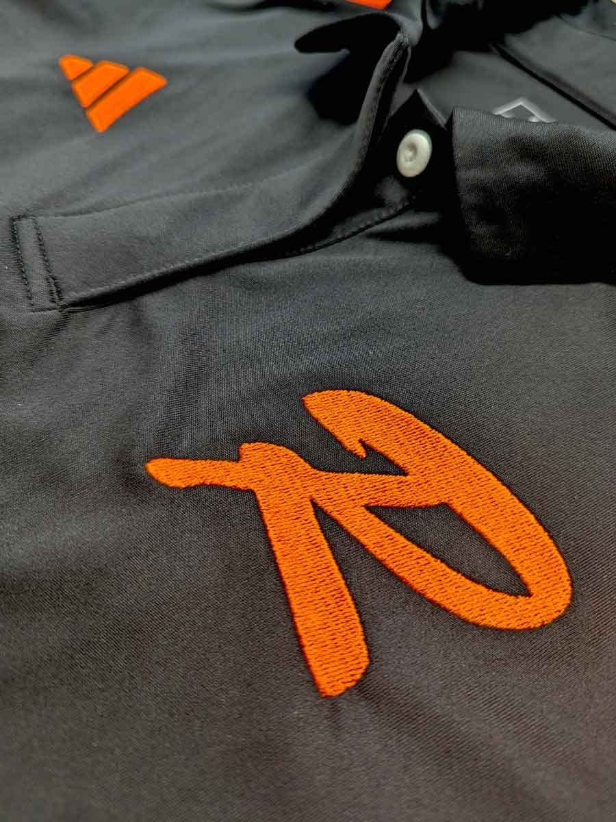 Nahaufnahme eines schwarzen Sporttaschenmaterials mit orangegesticktem Logo und weißen Knöpfen.