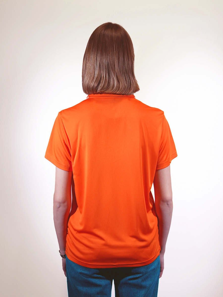 Rückansicht einer Frau mit braunen, schulterlangen Haaren, die ein orangefarbenes T-Shirt trägt und vor einem weißen Hintergrund steht.