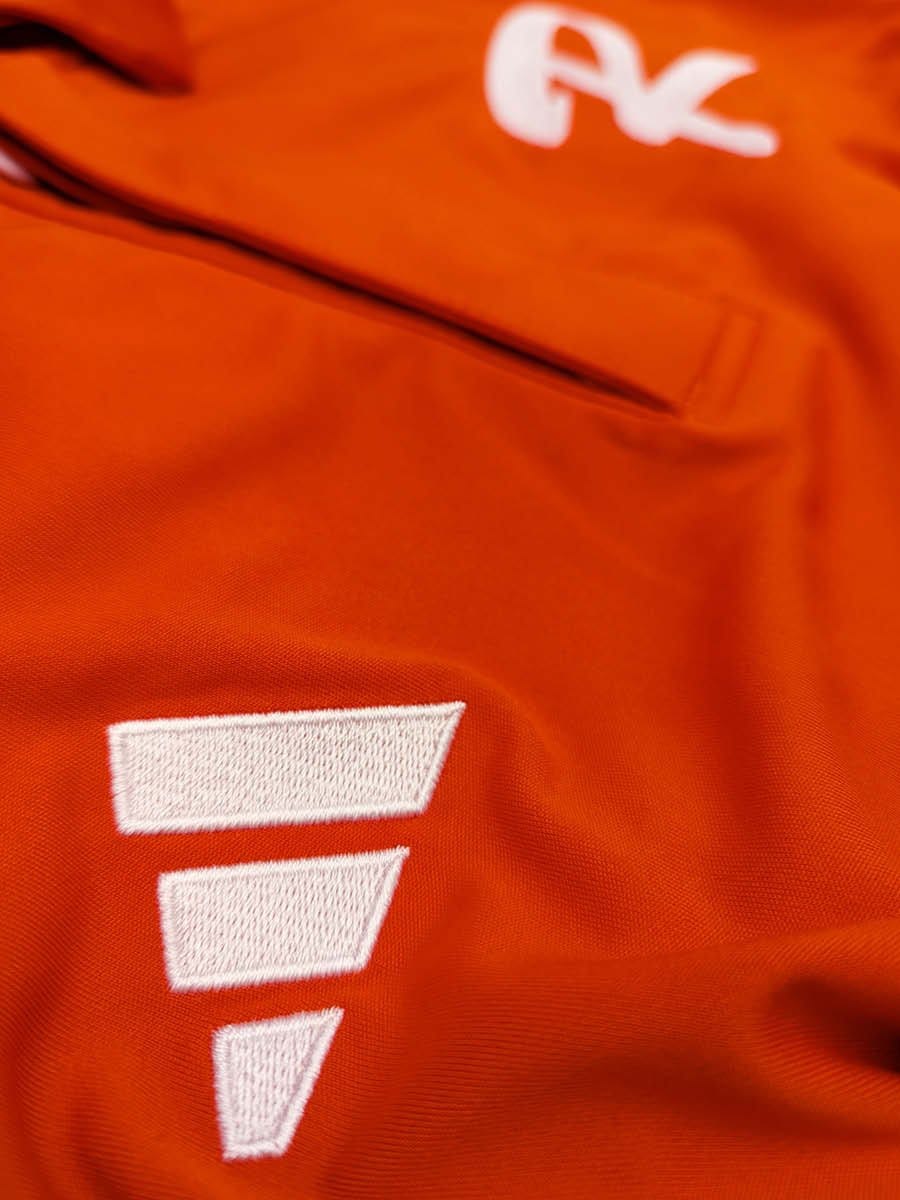 Nahaufnahme eines orangefarbenen Stoffes mit weißen, gestickten Buchstaben und einem weißen Logo.